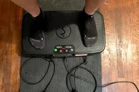 A person stands on top of the Sunny Health & Fitness Fitboard 2D Vibration Platform With Resistance Band