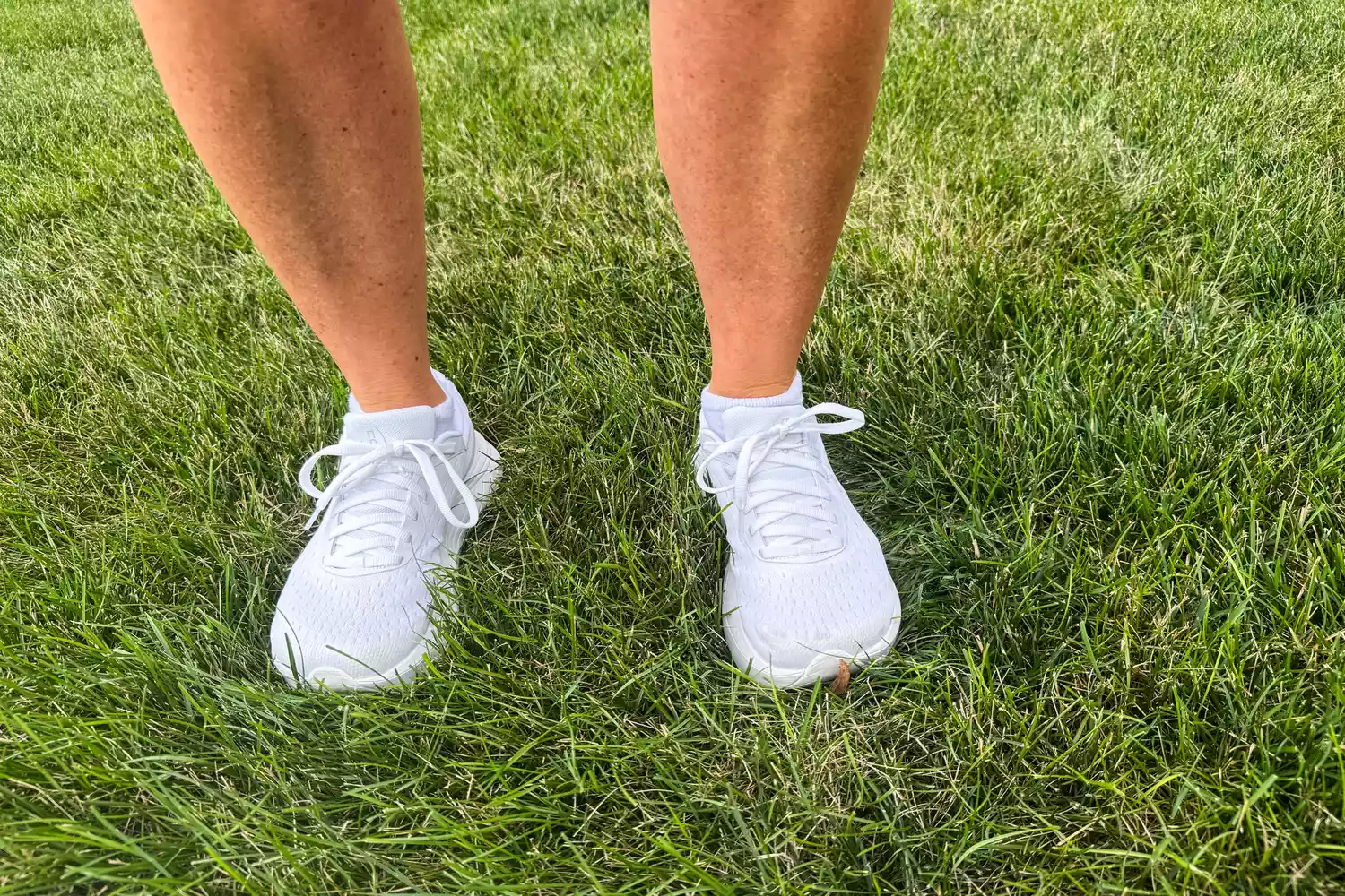 A person stands in grass while wearing the Topo Athletic Women's Atmos Running Shoes