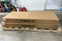 The pieces of the Torque Fitness' Free-Standing F9 Fold Away Functional Trainer in cardboard packaging