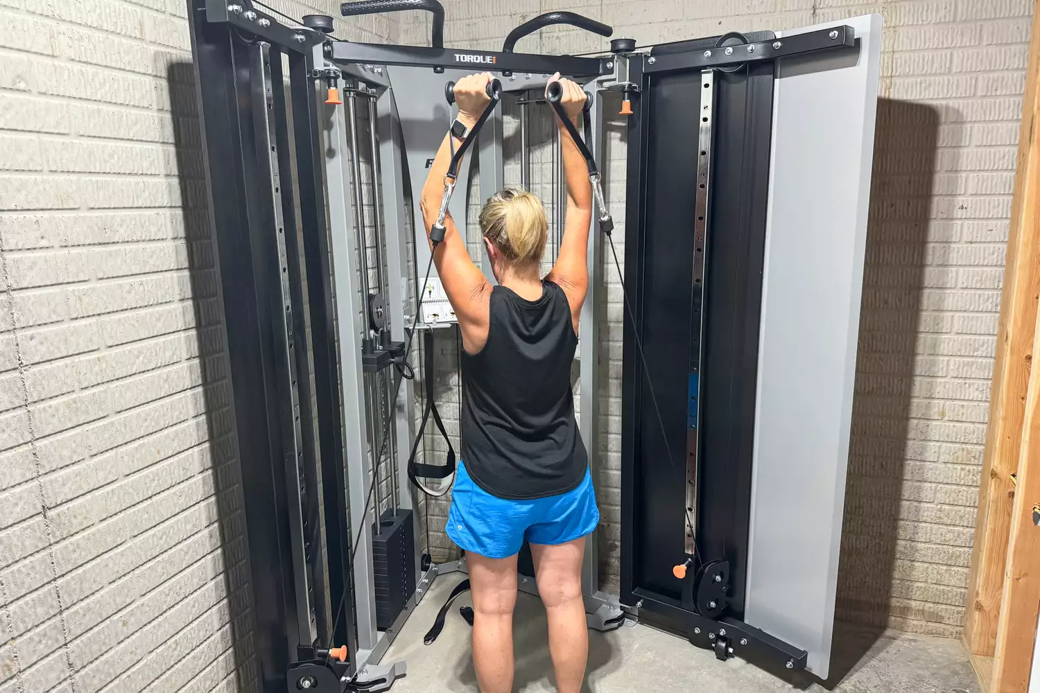 A person exercises on the dual adjustable cable pulleys of the Torque Fitness Free-Standing F9 Fold Away Functional Trainer