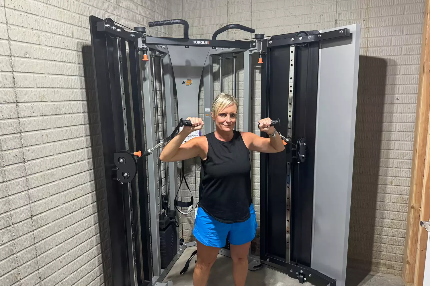A person uses the Torque Fitness Free-Standing F9 Fold Away Functional Trainer's swivel pulleys for exercise