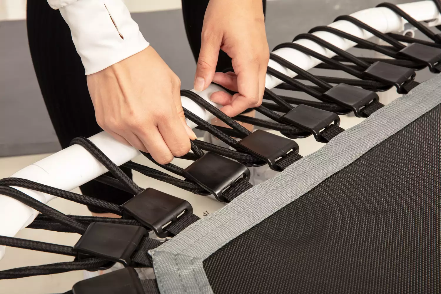 Person adjusting the spring strap buckle on an Acon 55in Trampoline Hexagon