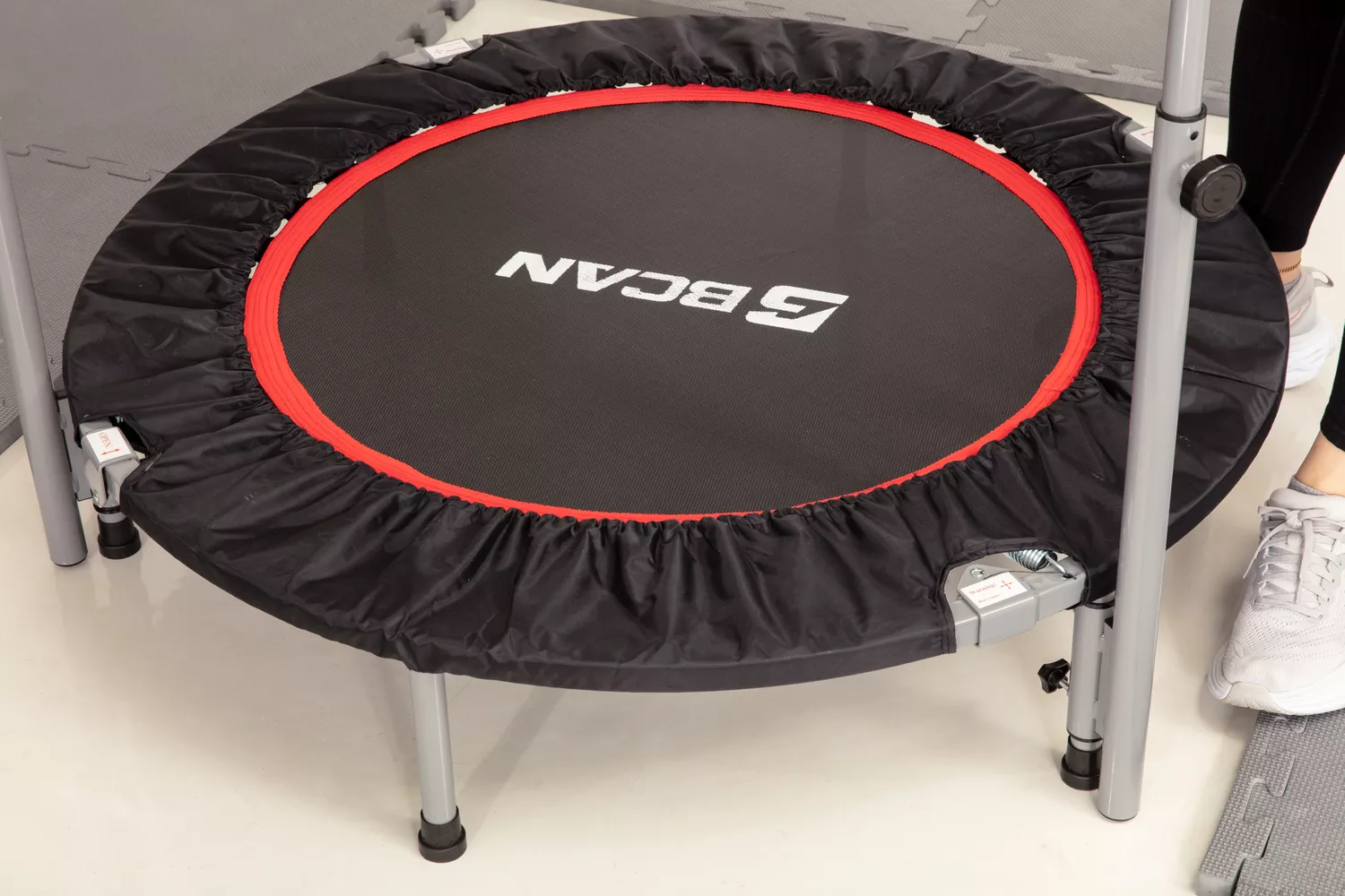 Person standing next to a BCAN Foldable Mini Trampoline surrounded by padded mats