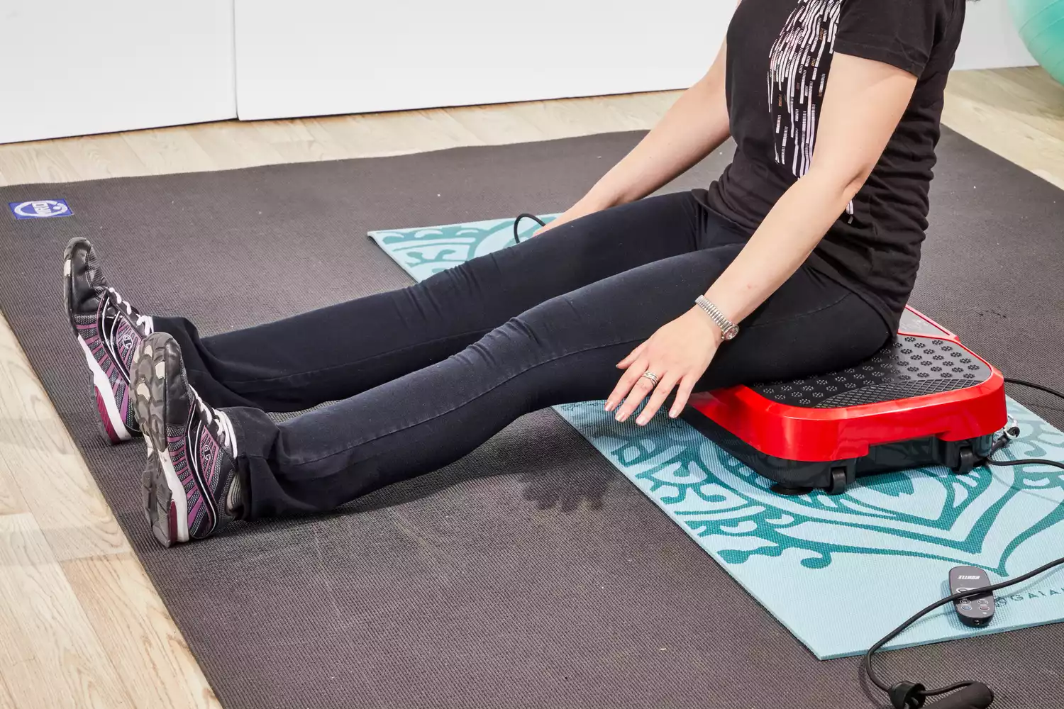 A person sits on the Hurtle Fitness Vibration Platform Machine