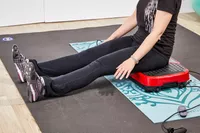 A person sits on the Hurtle Fitness Vibration Platform Machine