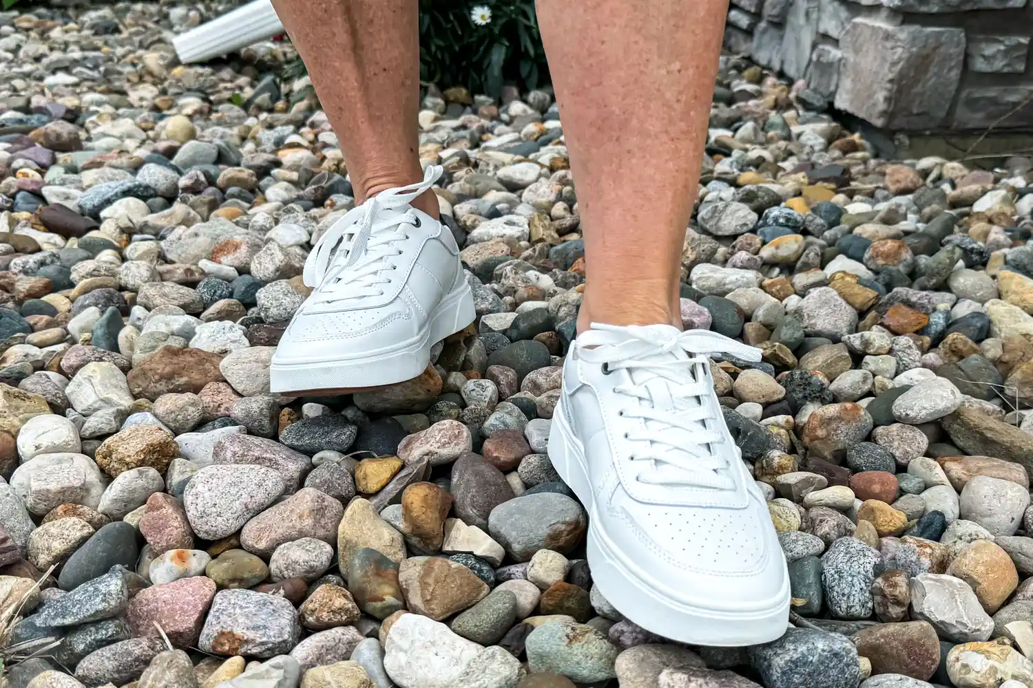 A person walks on pebbles while wearing the Vionic Women's Kimmie Court Sneakers