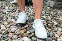 A person walks on pebbles while wearing the Vionic Women's Kimmie Court Sneakers