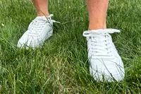 A person walks through grass while wearing the Vionic Women's Kimmie Court Sneakers