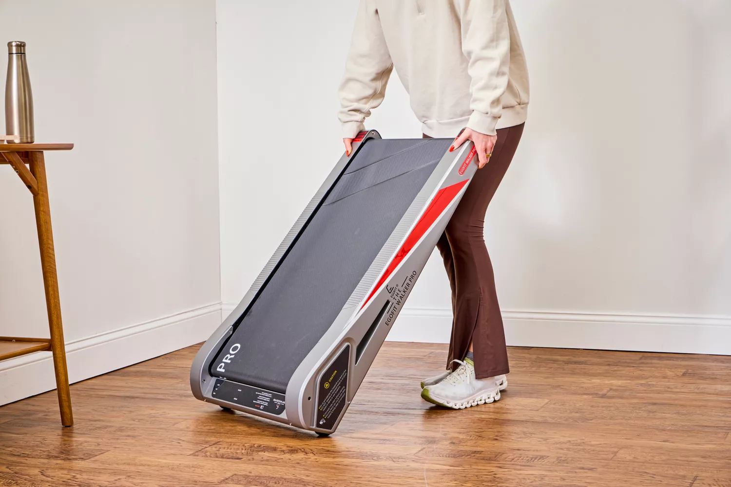 A person lifting the Egofit Walker Pro-M1 Treadmill off of a wooden floor