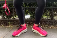 Feet wearing Nike Motiva Women's Walking Shoes on sidewalk near fence