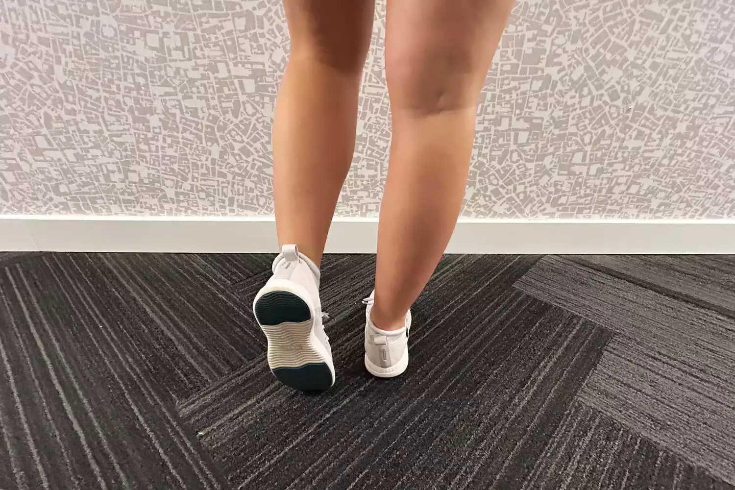 Feet wearing Vessi Cityscape Classic Waterproof Shoes with one lifted to reveal sole on carpet