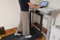 A person walks on the WalkingPad X25 Double-Fold Running Treadmill while typing on a laptop