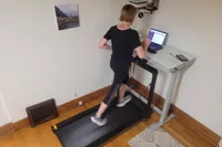 A person runs on the WalkingPad X25 Double-Fold Running Treadmill while looking at a laptop screen