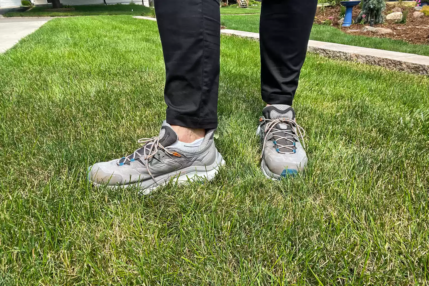 A person wears the Hoka Men's Kaha 2 Low GTX Hiking Shoes while walking through grass
