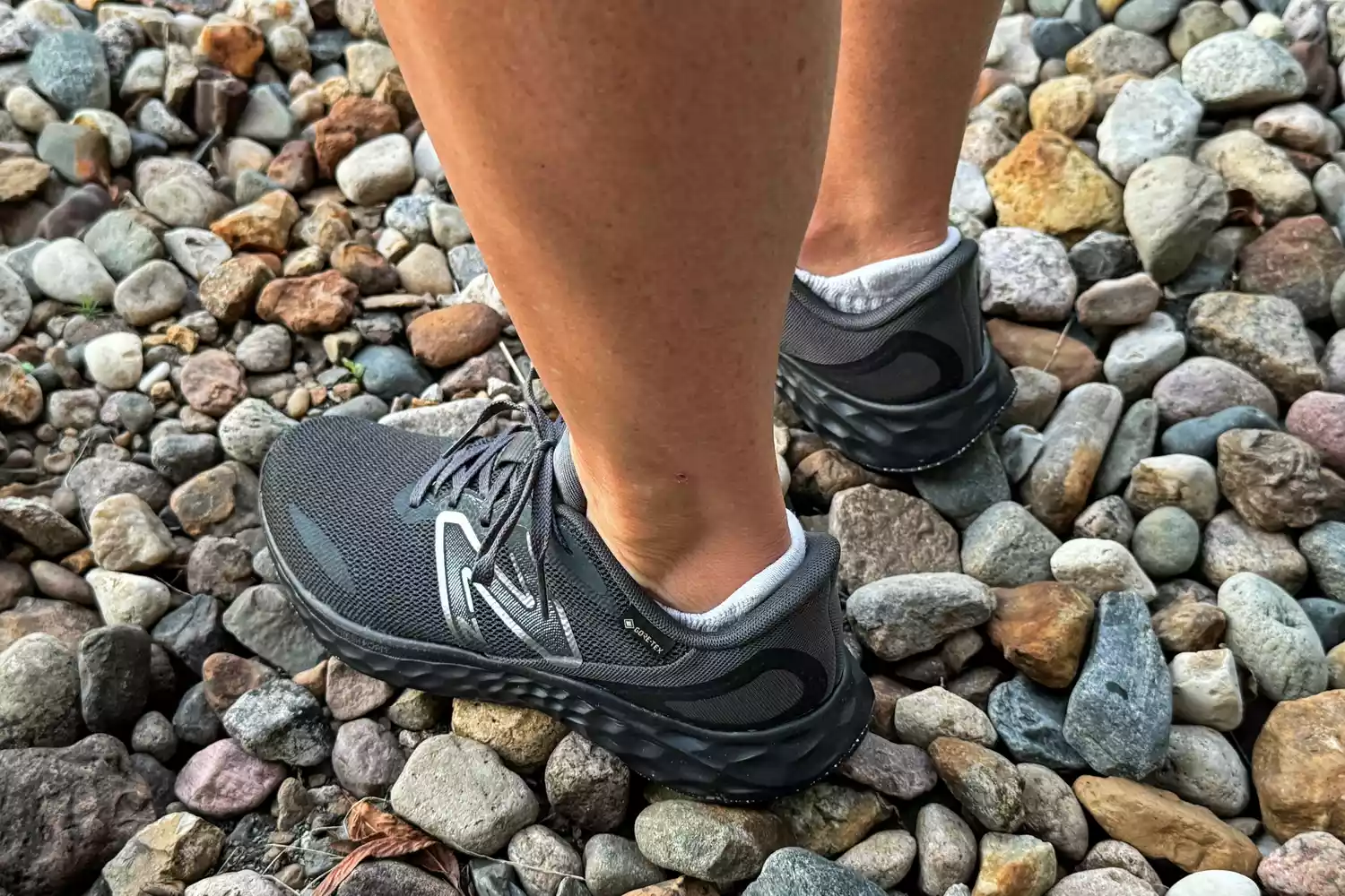 A person wears the New Balance Women's Fresh Foam Arishi v4 GTX Running Shoes while standing in pebbles