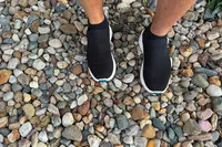 A person wears the Vessi Men's Everyday Move Slip Ons while standing in pebbles
