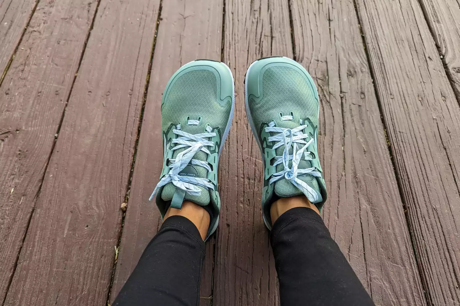 The Altra Lone Peak 8 Trail Running Shoes on legs resting on a wooden floor