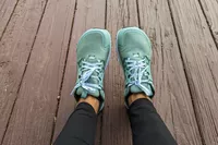 The Altra Lone Peak 8 Trail Running Shoes on legs resting on a wooden floor