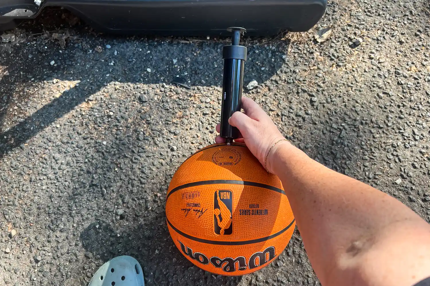 A person puts air in the Wilson NBA Authentic Outdoor Basketball