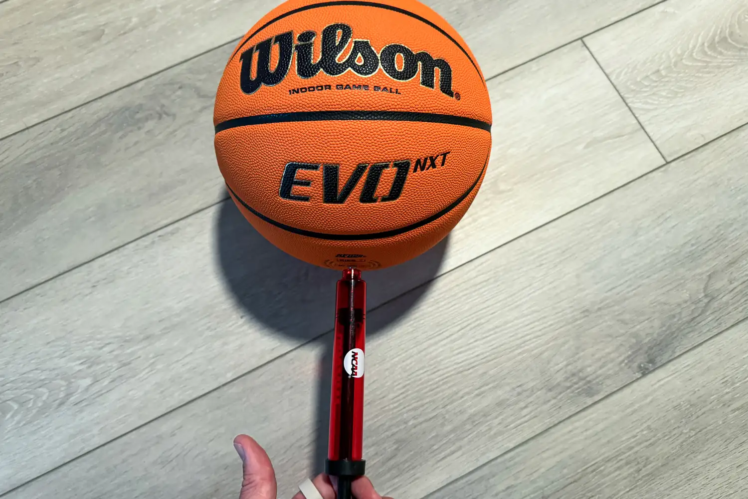 A person pumps air into the Wilson NCAA Evo NXT Game Basketball