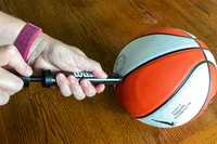 A person pumps air into the Wilson WNBA Authentic Outdoor Basketball