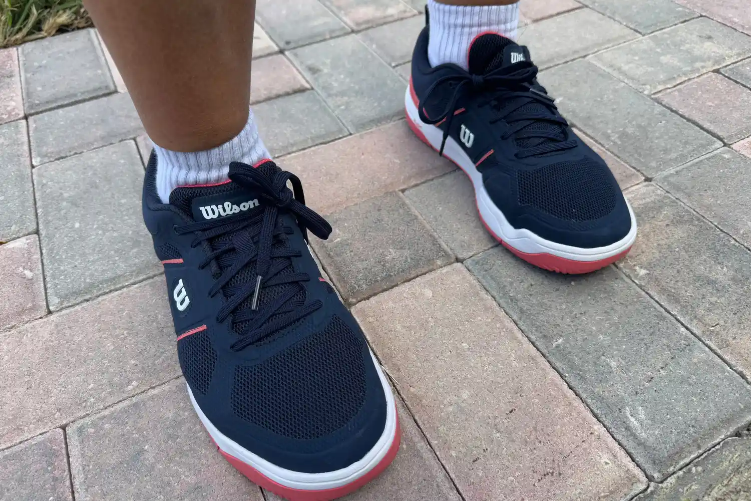 A person wears the Wilson Women's Pickle Pro Pickleball Shoe on brick