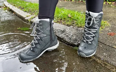 Closeup of waterproof hiking boots standing in a puddle.