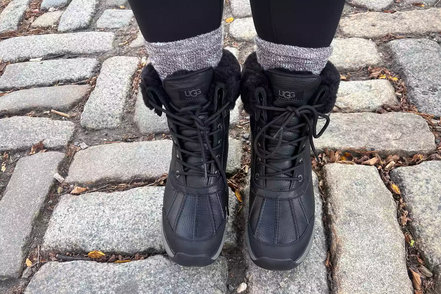 A person wears a pair of UGG Adirondack III Boots on a brick patio
