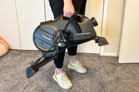 A person carries the YOSUDA YBM-2 Under Desk Bike Pedal Exerciser by the top handle