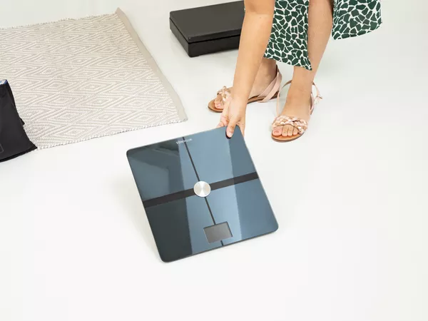Person picking up Withings Body Comp Smart Scale from floor