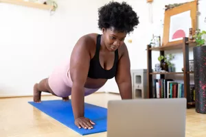 Woman doing mat Pilates at home following a fitness video online