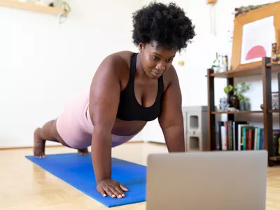 Woman doing mat Pilates at home following a fitness video online