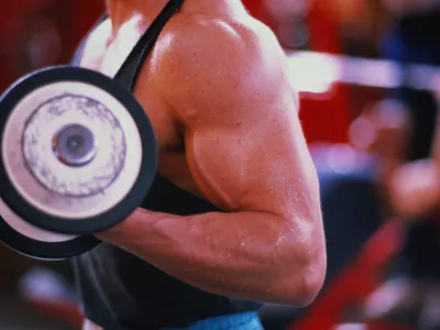 Young man exercising in gym, using dumbbell, mid section, close-up
