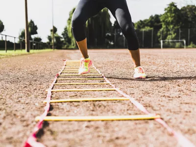 Young woman exercising on sports field with agility ladder